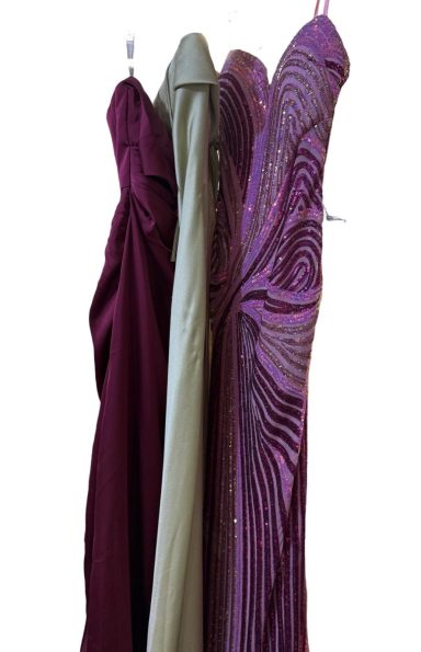 Three elegant dresses in burgundy, olive green, and sparkling purple hang side by side.
